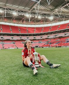 a woman sitting on the ground with a trophy in her hand and wearing soccer gear