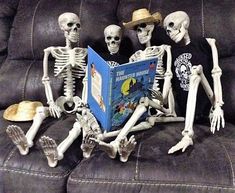 three skeletons sitting on a couch reading a book