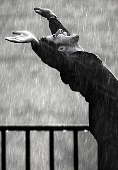 a man standing in the rain with his hands out to catch an object that he is holding