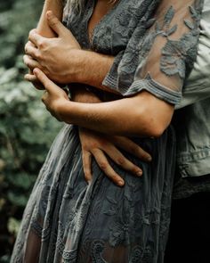 a man and woman embracing each other in front of some trees with their arms wrapped around them