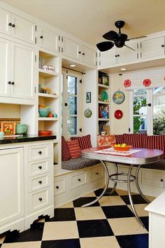 a kitchen with white cabinets and red striped cushions on the bench, along with built - in bookshelves