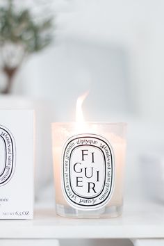 a candle sitting on top of a white table next to a box with a logo