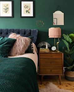 a bedroom with green walls and two pictures on the wall above the bed, next to a nightstand with a lamp