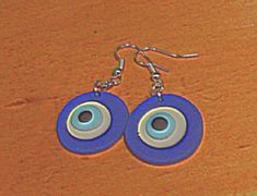 pair of earrings with blue and white circles on wooden table next to orange wall, closeup