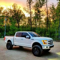 a white pickup truck parked in a parking lot next to some trees and bushes at sunset