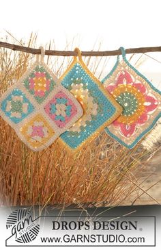 three crocheted squares hanging from a clothes line with grass in the foreground