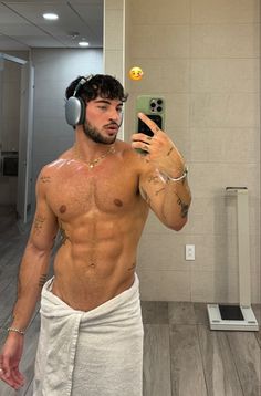 a man with headphones on taking a selfie in the bathroom while wearing a towel