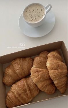 croissants in a box next to a cup of coffee