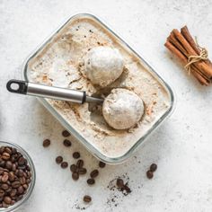 two scoops of ice cream with cinnamon sticks and coffee beans next to it on a white surface