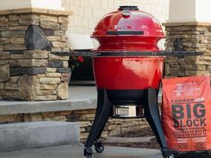 a big red bbq grill sitting on top of a sidewalk next to a bag