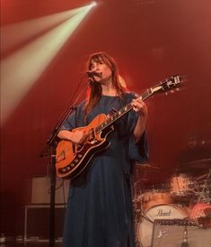 a woman standing in front of a microphone while holding a guitar