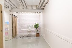 a white room with a computer on a desk and a potted plant in the corner