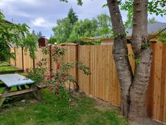 a wooden fence next to a tree with flowers on it and a picnic table in the foreground