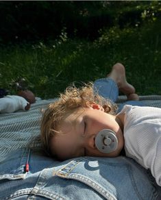 a little boy laying on top of a blanket next to a person with a pacifier in his mouth