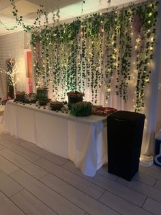 the table is set up with plants on it and lights hanging from the ceiling above