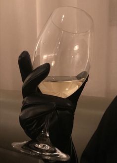 a hand that is holding a wine glass in it's right hand and the other hand has a black glove on it