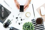 two hands holding a cell phone over a table with office supplies