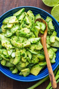 a blue bowl filled with cucumber and green beans next to sliced limes