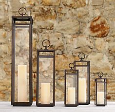 three black lanterns with candles sitting next to each other on a table in front of a stone wall