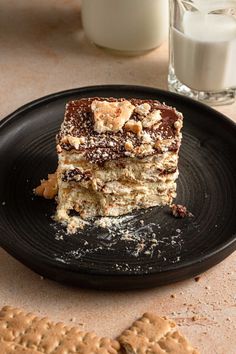 a piece of cake sitting on top of a black plate next to a glass of milk