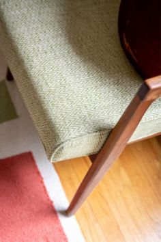 a cat sitting on top of a wooden chair next to a red and green rug