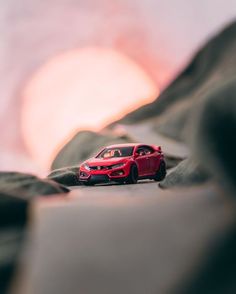 a red toy car sitting on top of a black surface next to the sun in the background