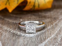 a white diamond ring sitting on top of a wooden table next to a yellow flower