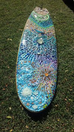 a colorful surfboard sitting in the grass on top of green grass with water droplets all over it