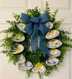 an easter wreath with painted eggs and greenery hangs on the front door, decorated with a blue bow