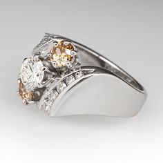 This lovely three-stone diamond ring is centered with one (1) round brilliant cut diamond set into a six- prong setting and flanked to each side by one (1) old European cut fancy light brown colored diamond set into a six-prong setting. The shoulders of the ring are accented with diamonds. One shoulder is bead set with nineteen (19) round single cut diamonds and one (1) round brilliant cut diamond. The other shoulder is channel set with five (5) round brilliant cut diamonds. The ring measures 13.1mm at the top, rises 6.8mm above the finger, tapering to 2.9mm wide and 1.1mm thick at the base of the shank. It is currently a size 6. Several of the diamonds are lightly chipped. Brown Diamond Ring Fine Jewelry, Classic Brown Diamond Jewelry, Brown Diamond Ring With Diamond Accents For Anniversary, Brown Diamond Ring With Accents For Anniversary, Anniversary Brown Diamond Ring With Accents, Elegant Brown Diamond Ring, Brown Prong-set Ring For Anniversary, Brown Prong Set Ring For Anniversary, Brown Rings With Prong Setting For Anniversary