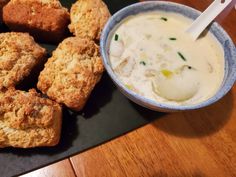 some biscuits and cream are on a black plate next to a bowl of soup with a spoon in it