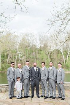 a group of men standing next to each other in front of a lake and trees