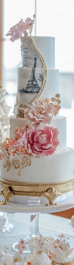 a three tiered wedding cake with pink flowers on the top and gold trimmings