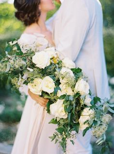 a bride and groom kissing in front of the camera with white flowers on their bouquet