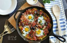 an iron skillet with eggs, tomatoes and olives in it on a table