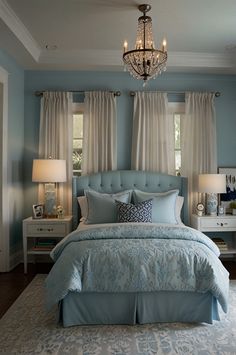 a bedroom with blue walls and curtains, a chandelier and two lamps on either side of the bed