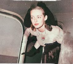 an old photo of a woman leaning out the back of a car door with her hands on her hips