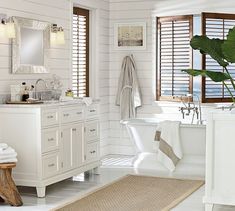 a white bathroom with wooden shutters and a large mirror on the wall above the bathtub