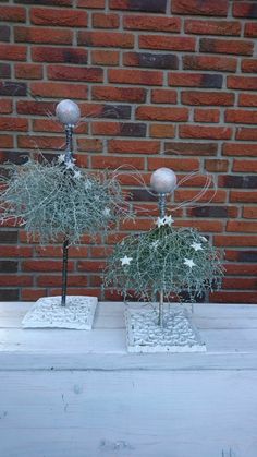 two silver vases sitting on top of a white table next to a brick wall