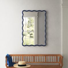 a wooden bench with a hat on top of it next to a wall mounted mirror