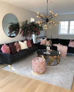 a living room filled with black couches and pink pillows on top of a rug