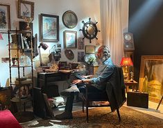 an older man sitting in a chair next to a desk with lots of pictures on the wall