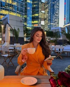 a woman sitting at a table with a cup of coffee in her hand and looking down