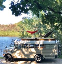 an old bus is parked next to the water with a kayak on it's roof