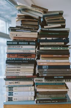 a stack of books sitting on top of a wooden shelf in front of a window