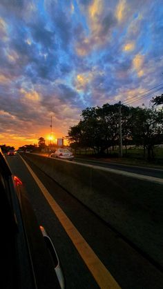 the sun is setting behind some clouds in the sky as cars drive down the road