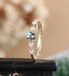 an engagement ring with blue and white diamonds on top of a wooden table in front of a flower arrangement