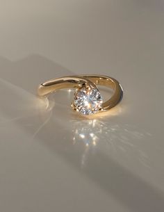 a gold ring with a single diamond on it's side, sitting on a white surface