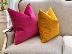 three different colored pillows sitting on top of a white couch next to a potted plant