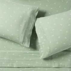 two pillows and one pillow case with white flowers on green sheets in a hotel room